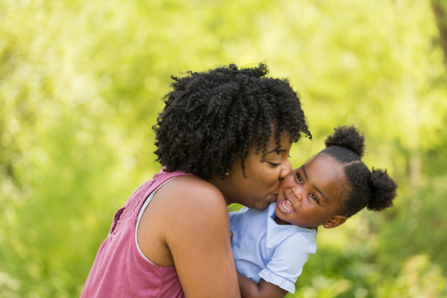 A black woman hugs and kisses a young girl who is smiling outside on the Informed Pregnancy Blog