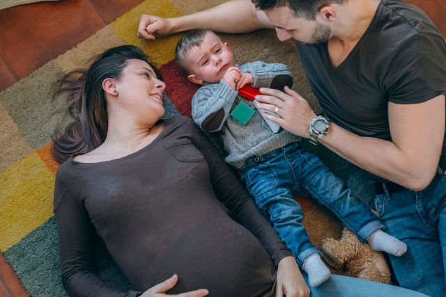 Pregnant mom lays on floor with new big brother and dad