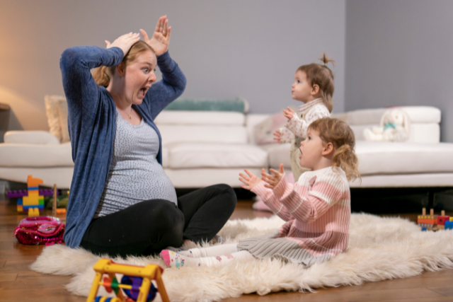 Pregnant mom sits on floor singing with two toddler big sisters