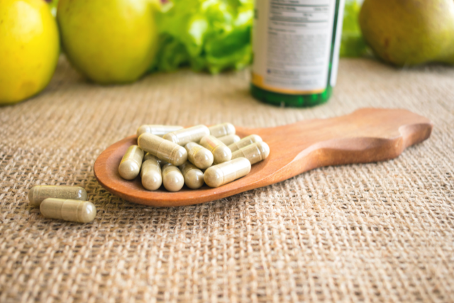 Herbal supplement gel caps in a shallow decorative wooden spoon on The Informed Pregnancy Blog