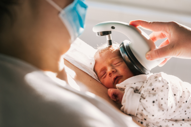 Infant help my by mother while hearing test is administered in hospital