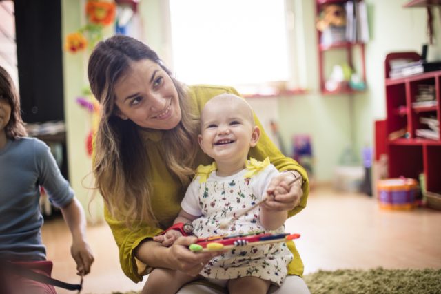 Baby sitting on woman's lap holding toy at daycare