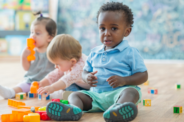 toddlers at daycare on floor with toys, little boy is sad while looking at camera
